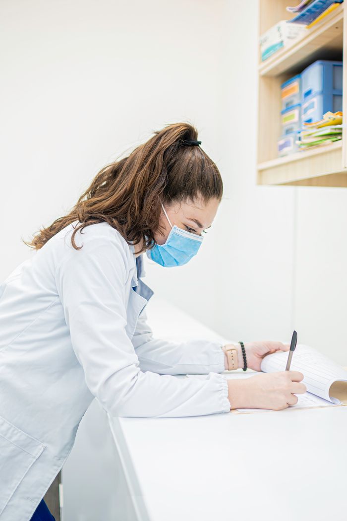 A nurse in medical uniform writes on documents in a healthcare facility.